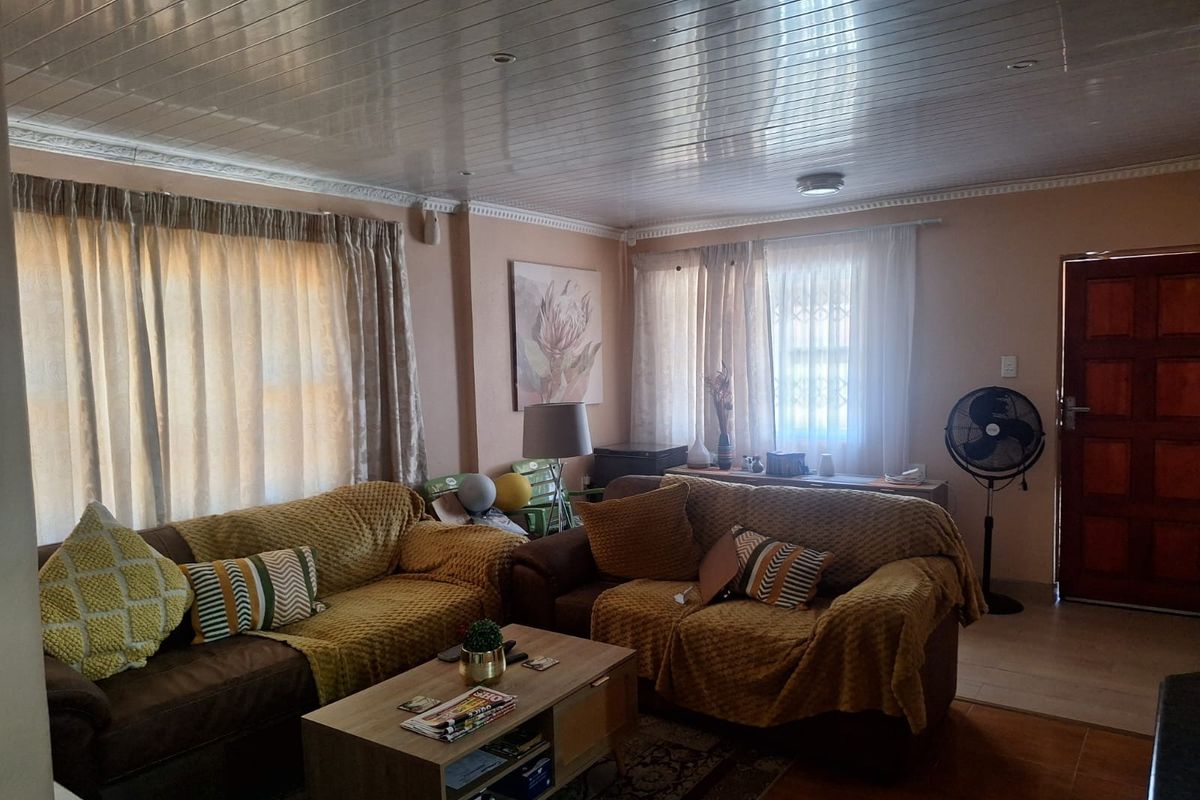 A living room featuring a tongue and groove ceiling, tiled flooring, and a timber entrance door, offering a comfortable and functional living space.