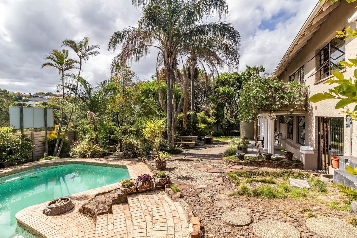 Rear exterior view featuring a swimming pool, paved patio area, and established garden with mature palm trees and a water tank.