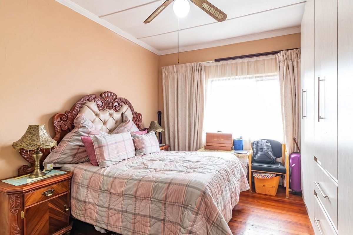 A cozy bedroom featuring warm-toned walls, polished hardwood flooring, built-in storage cupboards, and a ceiling fan.