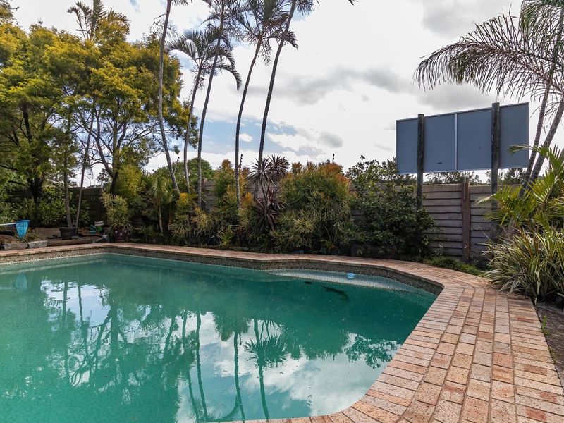 Outdoor pool area featuring a swimming pool with brick coping, surrounded by established garden landscaping and a timber boundary fence.