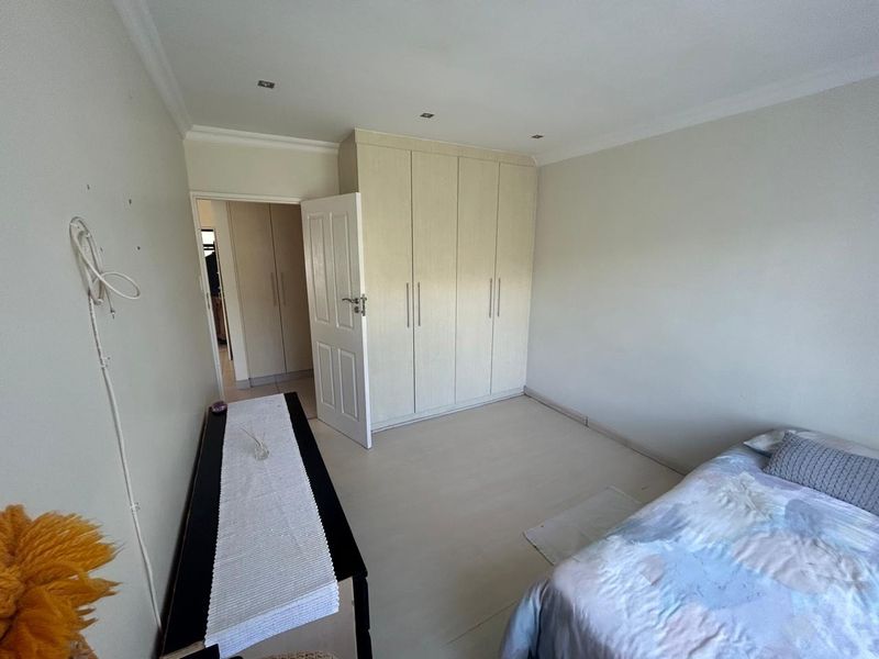 A bedroom featuring built-in cupboards, recessed downlighting, and neutral flooring, offering a functional space with potential for cosmetic updates.