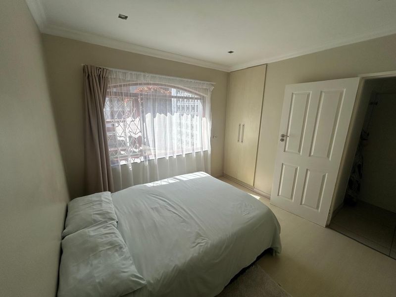 A functional bedroom featuring built-in cupboards, recessed downlighting, and an arched window with security bars.