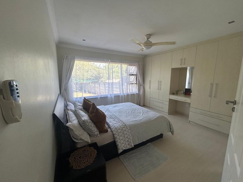 Spacious bedroom featuring extensive built-in cabinetry with an integrated vanity, ceiling fan, and large window providing natural light.