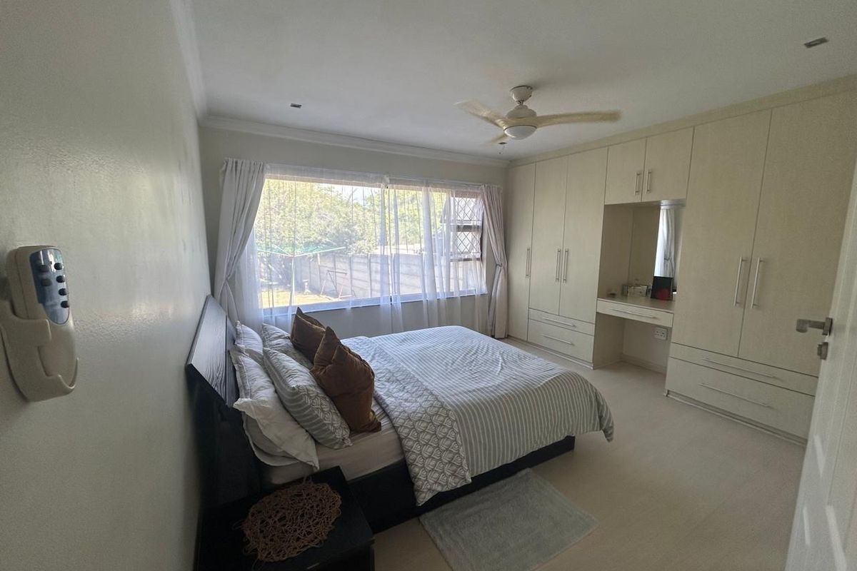 Spacious bedroom featuring extensive built-in cabinetry with an integrated vanity, ceiling fan, and large window providing natural light.