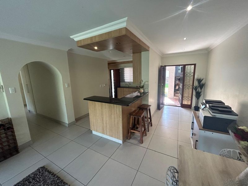 Open plan living area featuring a breakfast bar, tiled flooring, and a distinctive recessed ceiling feature with integrated lighting.