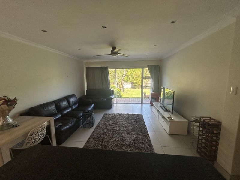 Spacious living room featuring tiled flooring, recessed lighting, and a ceiling fan, with direct access to the rear garden through a sliding glass door.