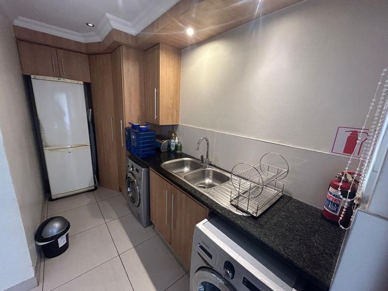 A functional kitchen featuring laminate cabinetry, granite countertops, a double bowl stainless steel sink, and tiled flooring with integrated appliance spaces.