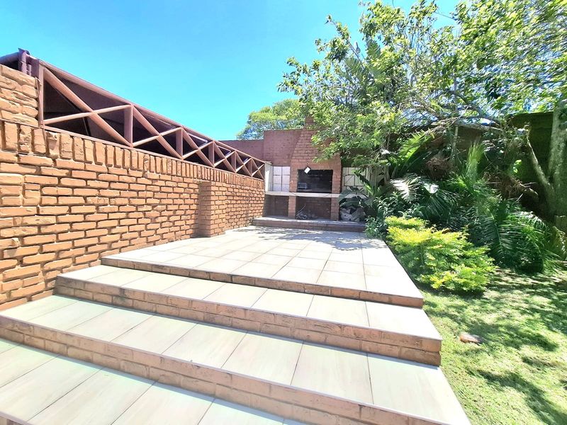 Outdoor patio area featuring a built-in brick braai, tiled flooring, and a brick boundary wall with a wooden lattice screen.