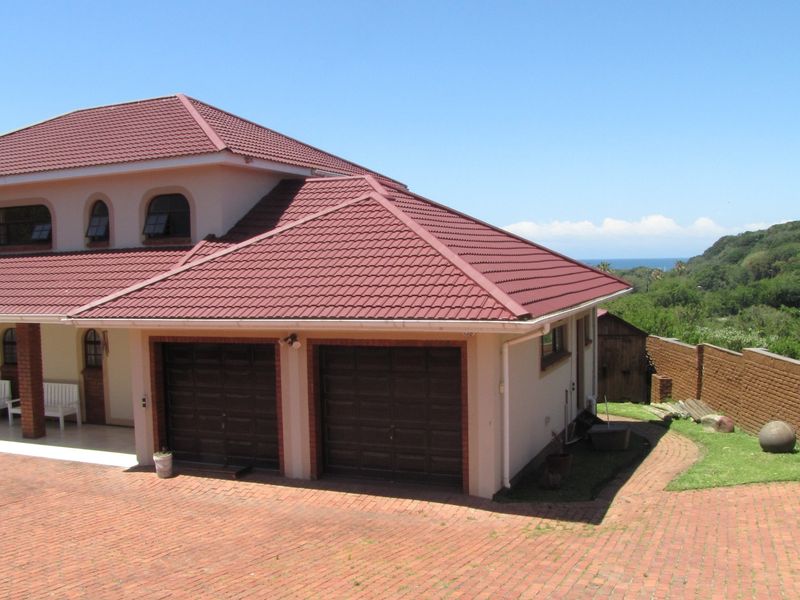Front view of a double-story house featuring a double garage, tiled roof, and a brick-paved driveway with surrounding garden and boundary wall.
