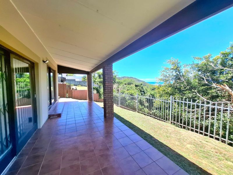 A spacious covered patio featuring tiled flooring and brick pillars, offering an open outlook over the garden and surrounding landscape.