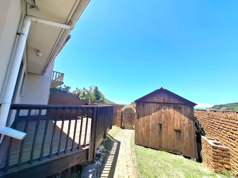 Rear exterior view featuring a wooden deck, brick boundary walls, a garden shed, and a brick pathway leading to a wooden gate.