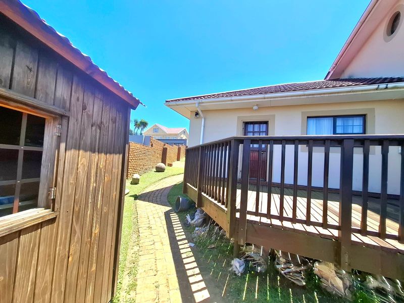 A rear exterior view featuring a wooden deck, a brick pathway leading along the side of the house, and a detached wooden storage shed.