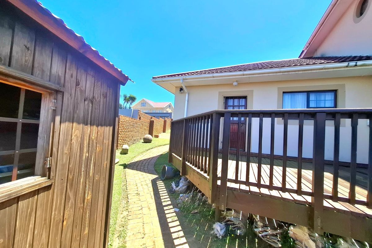 A rear exterior view featuring a wooden deck, a brick pathway leading along the side of the house, and a detached wooden storage shed.