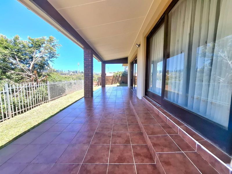 A spacious covered patio featuring tiled flooring and brick pillars, providing direct access to the garden through large sliding glass doors.
