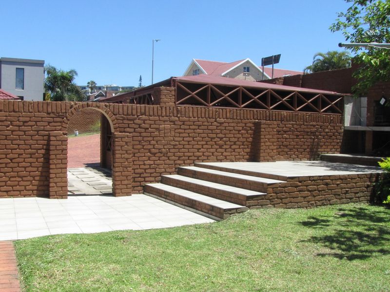 Outdoor patio area featuring a brick boundary wall with an arched entrance, raised steps, and a built-in braai, set within a garden space.