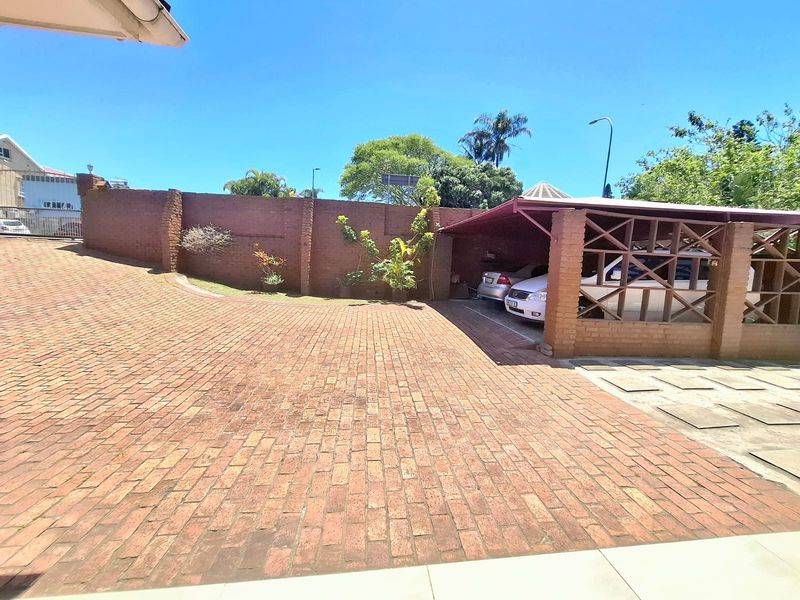 A paved brick driveway leading to a covered carport structure with brick pillars and a surrounding brick boundary wall.