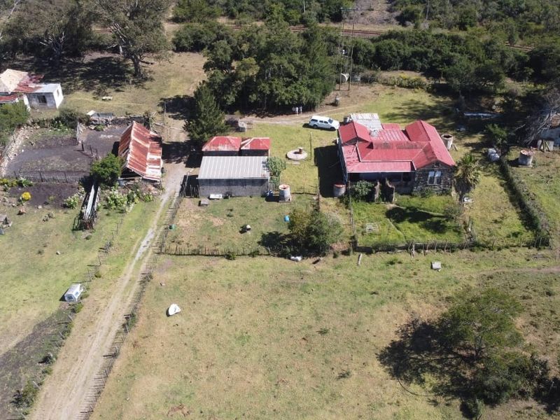 Aerial view of a rural farm property featuring a main stone residence with a red metal roof, multiple outbuildings, and surrounding pasture land.