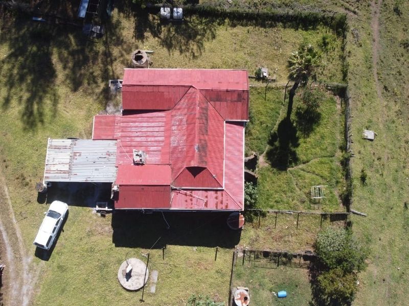 Aerial view of a farm property featuring a main dwelling with a red corrugated metal roof, surrounding fenced grounds, and outdoor water infrastructure.