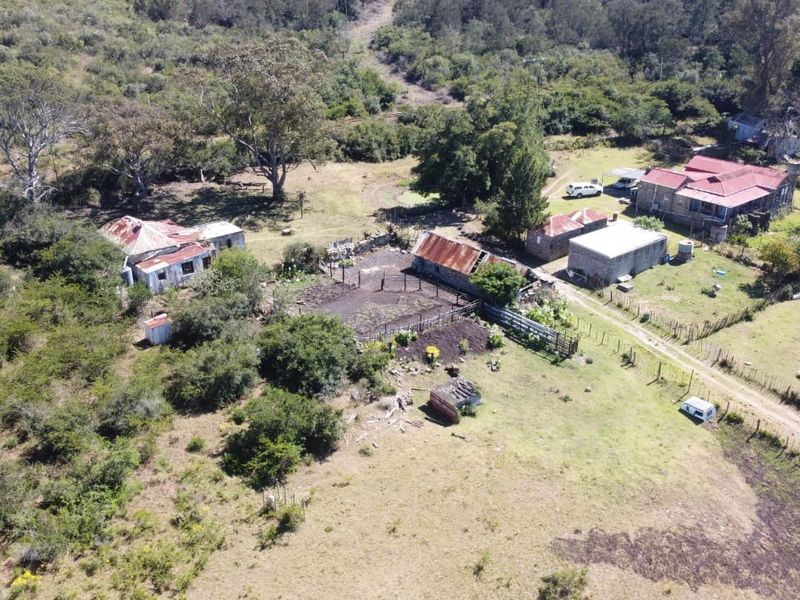 Aerial view of a rural farm property featuring multiple outbuildings, corrugated metal roofing, and extensive surrounding land with established fencing and access paths.