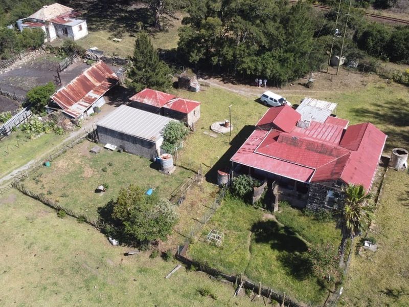 Aerial view of a farm property featuring a main residence with a red metal roof, multiple outbuildings, and surrounding rural land.