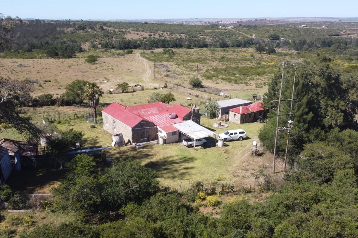 Aerial view of a rural farm property featuring a main stone dwelling with a metal roof, multiple outbuildings, and surrounding agricultural land.