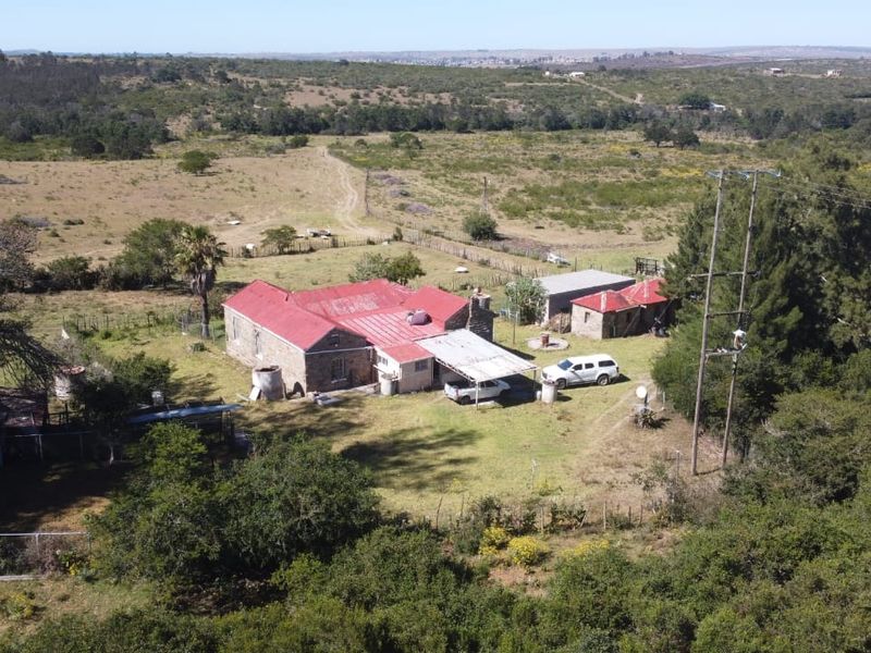 Aerial view of a rural farm property featuring a main stone dwelling with a metal roof, multiple outbuildings, and surrounding agricultural land.