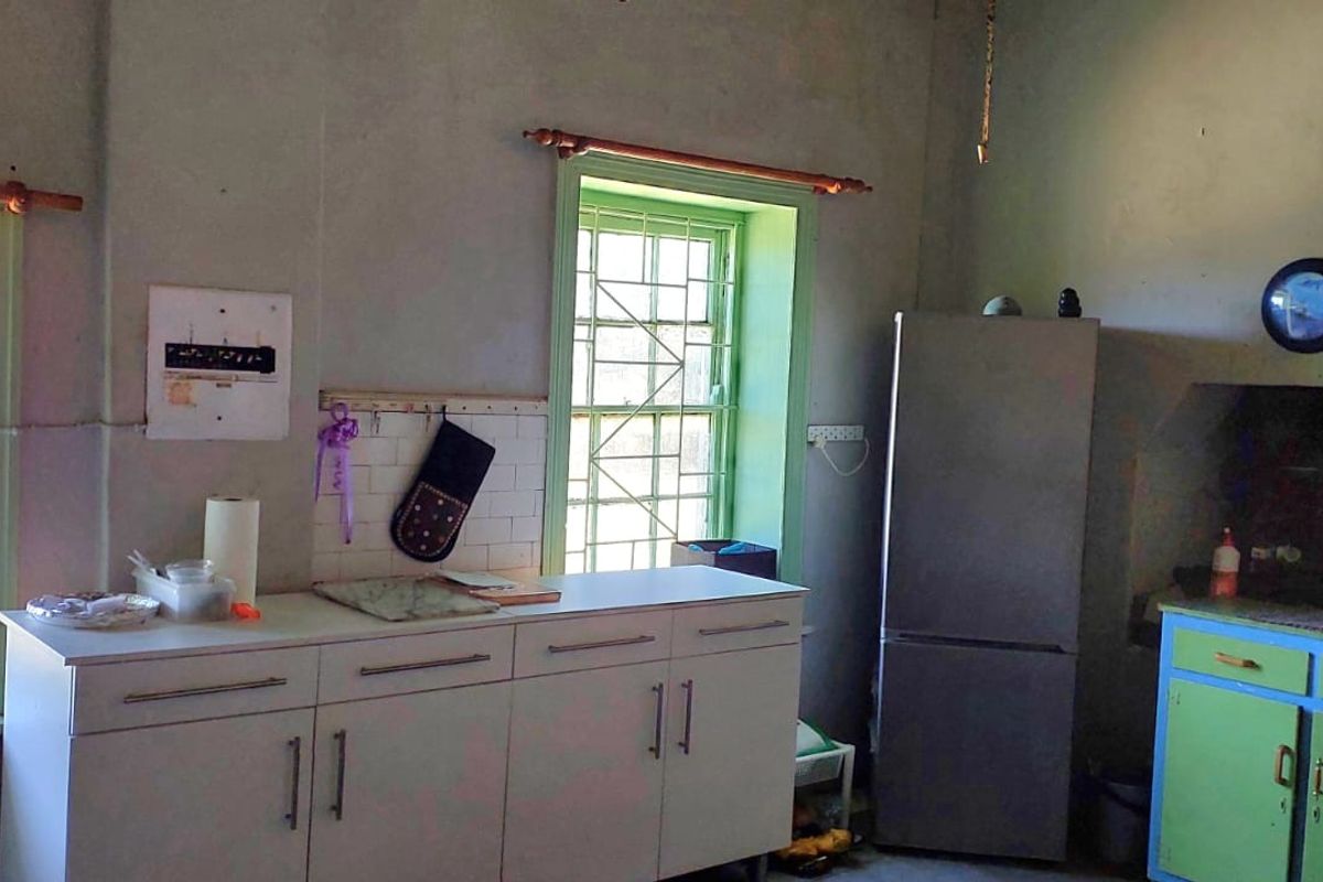A dated kitchen area featuring built-in cabinetry, tiled backsplash, and security bars on the windows, requiring cosmetic updates to improve the overall aesthetic.