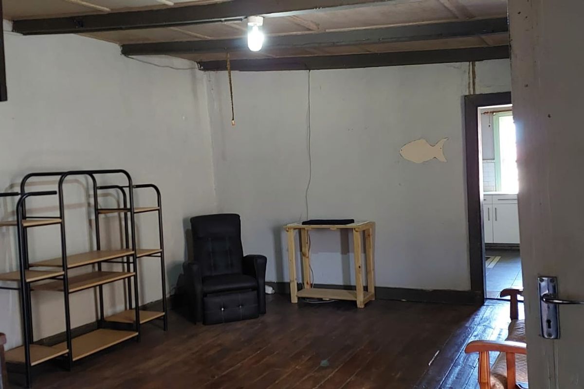 A sparsely furnished living area featuring exposed timber ceiling beams and original timber flooring, requiring cosmetic updates to improve the overall aesthetic.