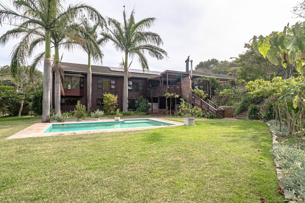 Rear view of a two-story farm residence featuring timber cladding, a raised deck with external stairs, and a swimming pool set in a garden.