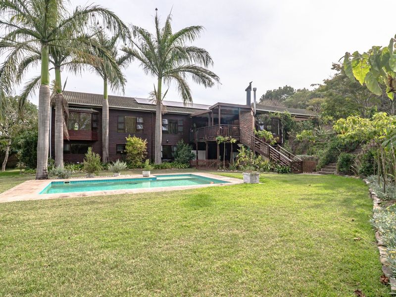 Rear view of a two-story farm residence featuring timber cladding, a raised deck with external stairs, and a swimming pool set in a garden.