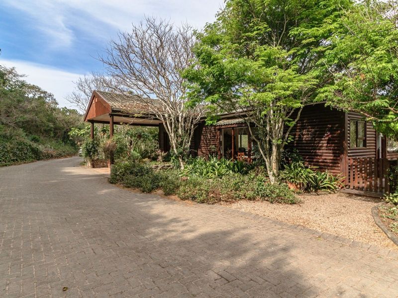 A charming log cabin style home featuring a paved driveway, covered entrance, and established garden surroundings in a peaceful setting.