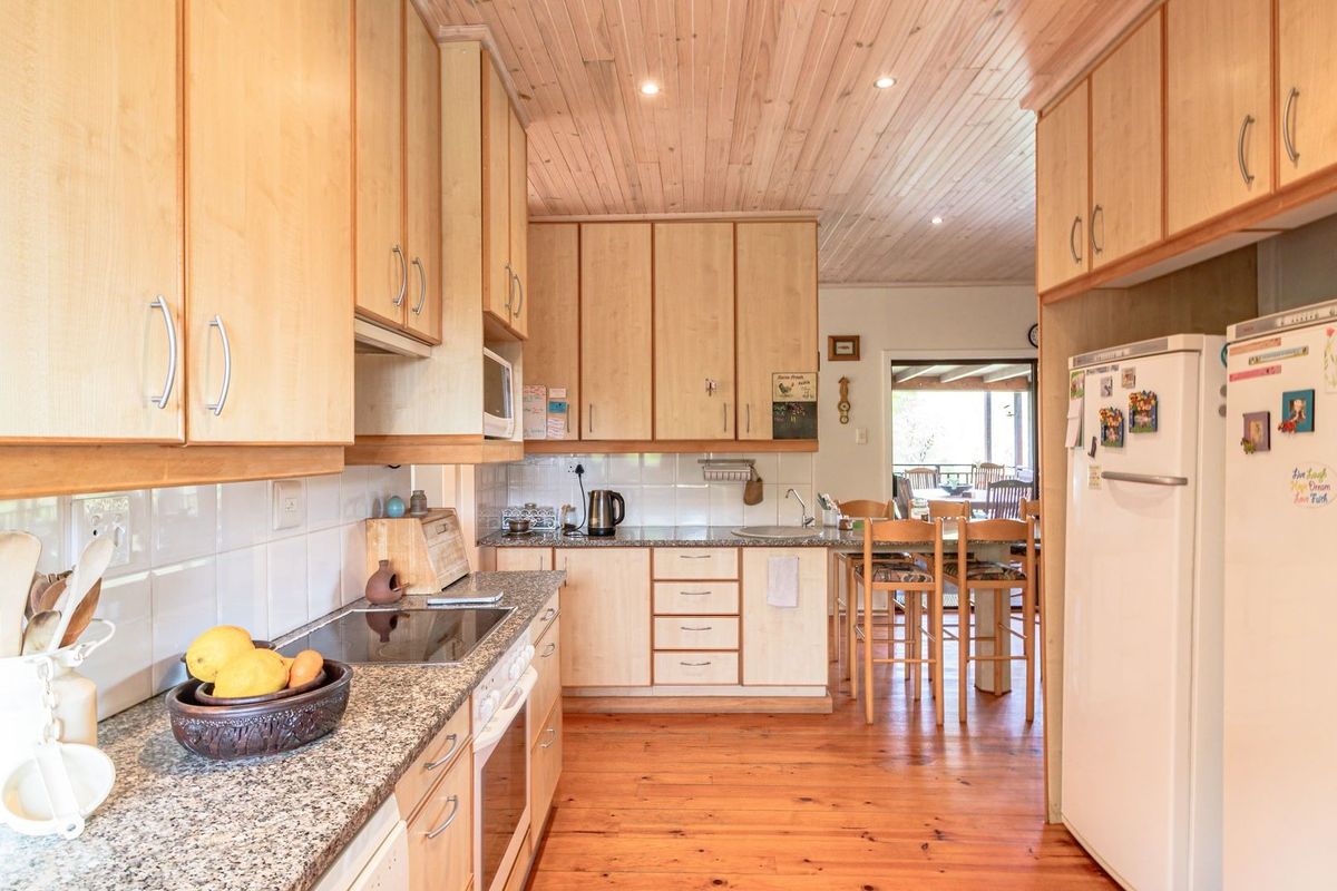 Functional kitchen featuring light wood cabinetry, granite countertops, electric hob, and warm timber flooring, with an open flow to the adjacent dining area.
