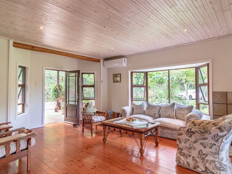 Spacious living room featuring warm hardwood flooring, a timber-clad ceiling, a cozy fireplace with a tiled hearth, and large bay windows overlooking the garden.