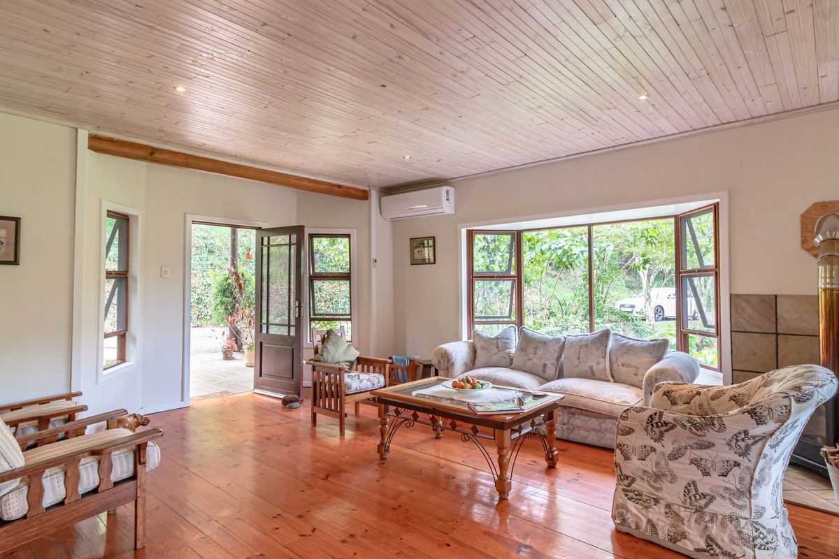 Spacious living room featuring warm hardwood flooring, a timber-clad ceiling, a cozy fireplace with a tiled hearth, and large bay windows overlooking the garden.