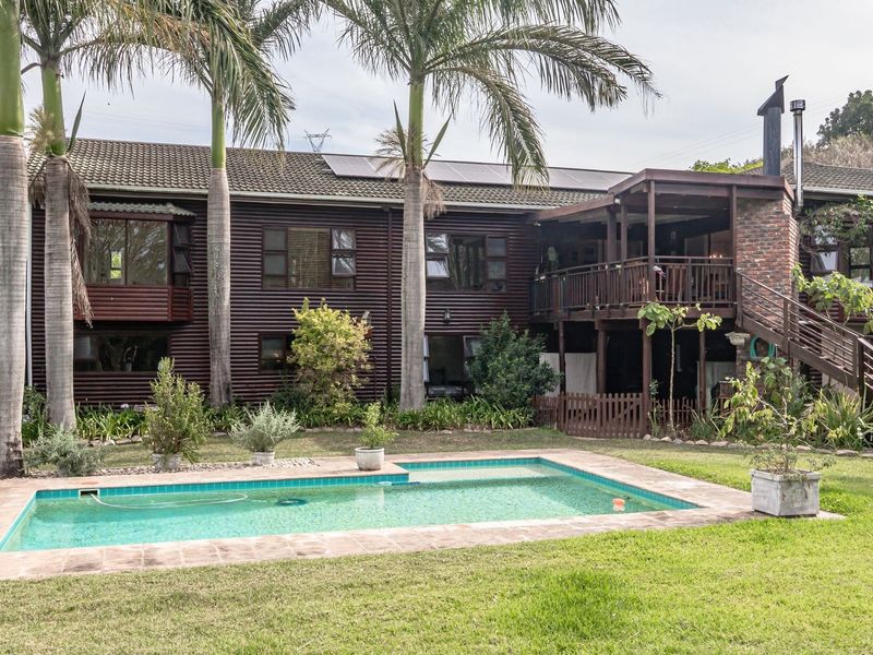 Rear view of a multi-level farm property featuring a swimming pool, raised wooden deck, external staircase, and solar panels on a tiled roof.