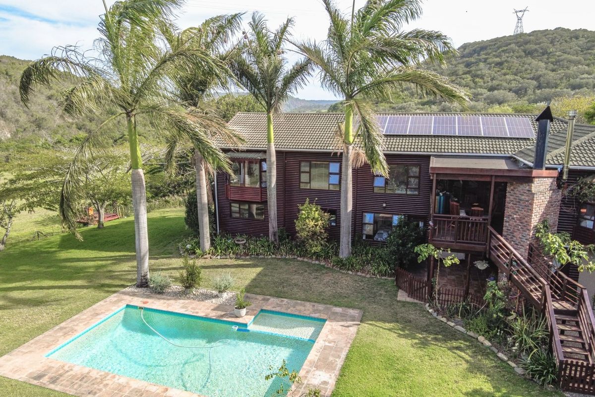Aerial view of a timber-clad farmhouse featuring a swimming pool, raised wooden deck, and roof-mounted solar panels set against a scenic rural landscape.