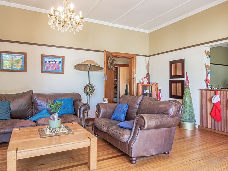 A spacious living room featuring polished timber flooring, classic picture rails, and a decorative crystal chandelier, offering a warm and traditional atmosphere.