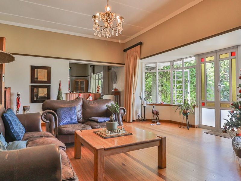Spacious living room featuring hardwood flooring, a classic crystal chandelier, and a large bay window with access to the garden.