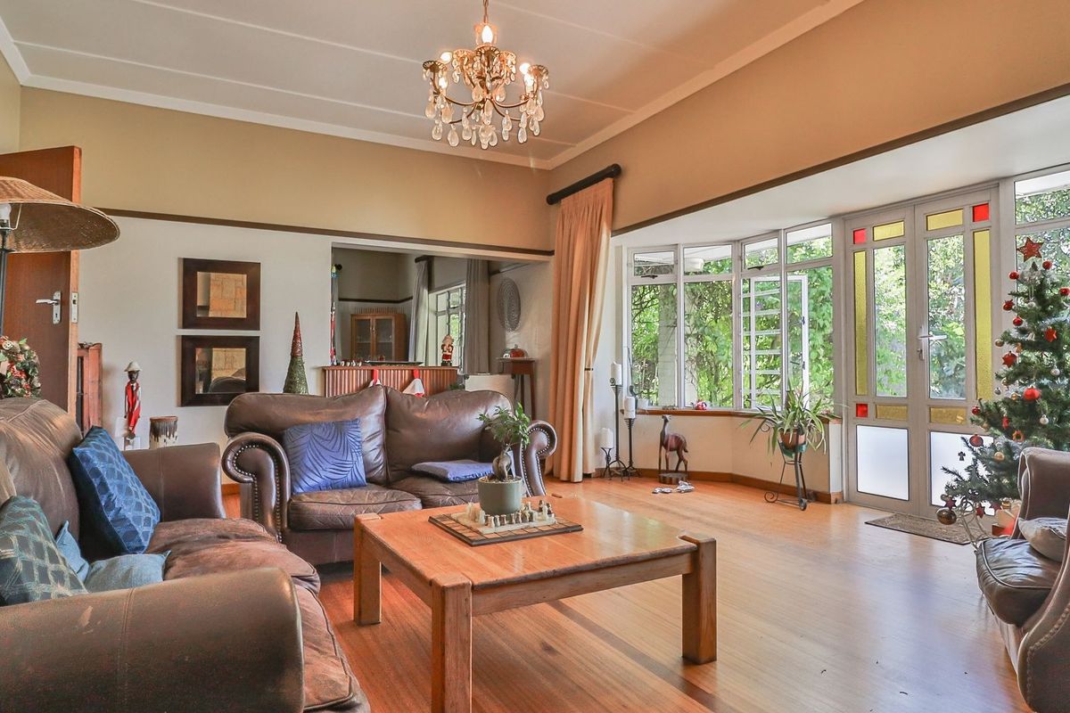Spacious living room featuring hardwood flooring, a classic crystal chandelier, and a large bay window with access to the garden.