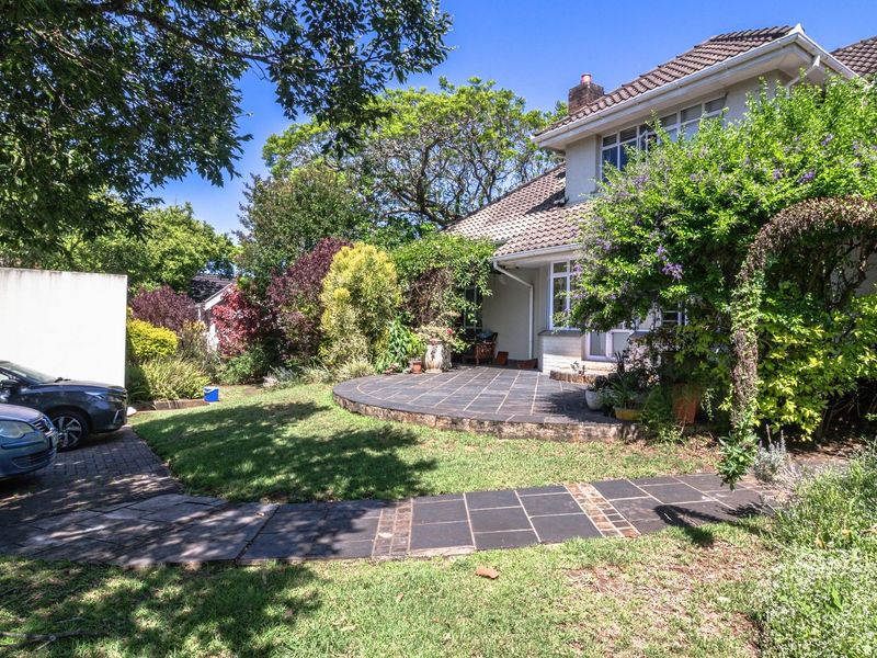 Rear view of the property featuring a tiled patio area, paved garden walkway, and established landscaping.