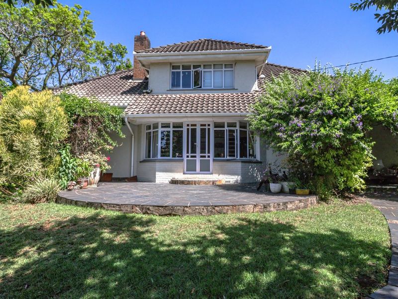 Rear view of the house featuring a stone patio, landscaped garden, and classic tiled roof architecture.