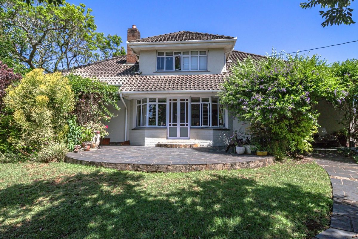 Rear view of the house featuring a stone patio, landscaped garden, and classic tiled roof architecture.