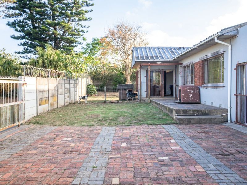 Rear exterior view featuring a brick paved driveway, concrete patio, and secure boundary wall with razor wire.