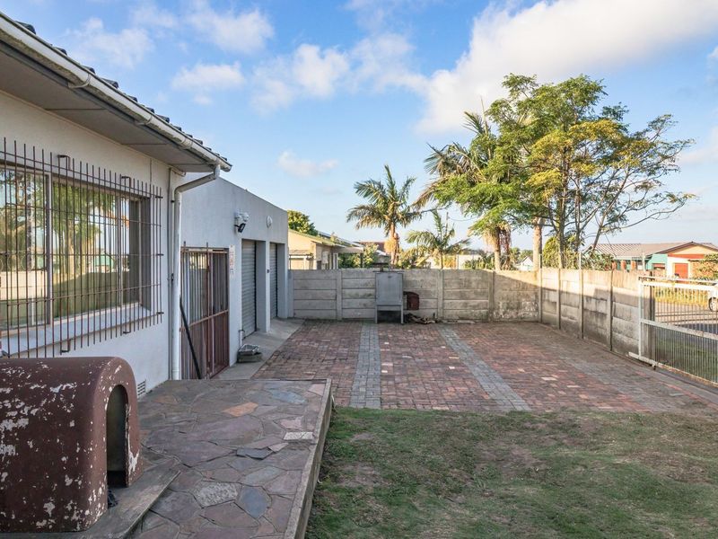A rear exterior view featuring a paved courtyard, built-in braai, and secure boundary walling, providing a functional outdoor space.