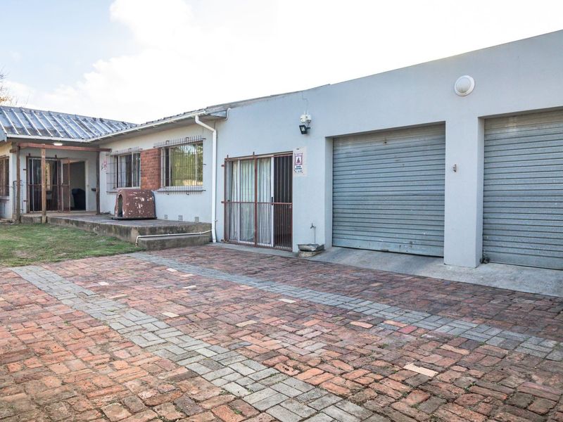 Rear exterior view featuring a brick paved driveway, double garage with metal roller doors, and a concrete patio area.