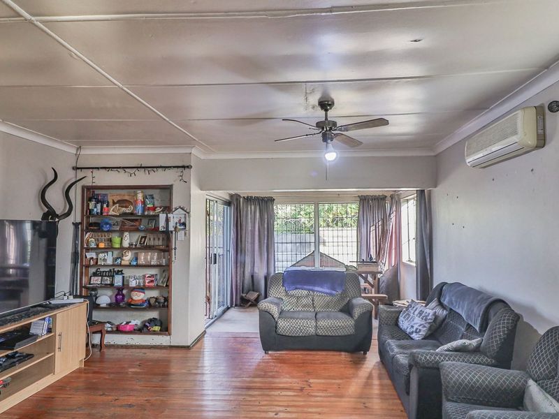 Spacious living room featuring timber flooring, a ceiling fan, wall-mounted air conditioning, and built-in shelving, with direct access to the outdoor area via sliding doors.