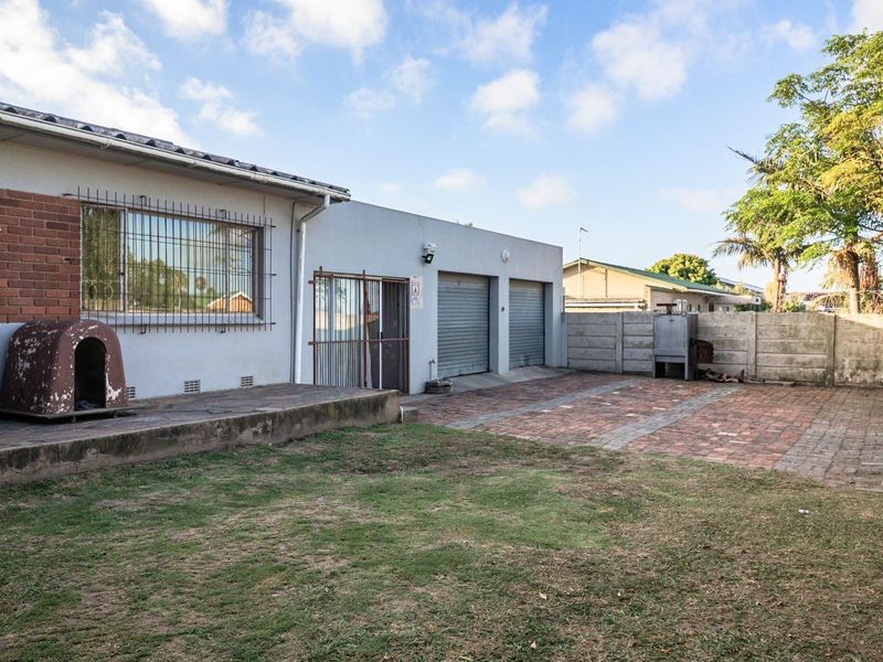 Rear exterior view featuring a paved patio area, double garage access, built-in braai, and a fenced garden space.