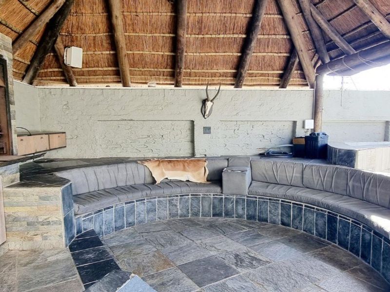 Covered outdoor entertainment area featuring a thatched roof, built-in braai, and curved stone seating area.