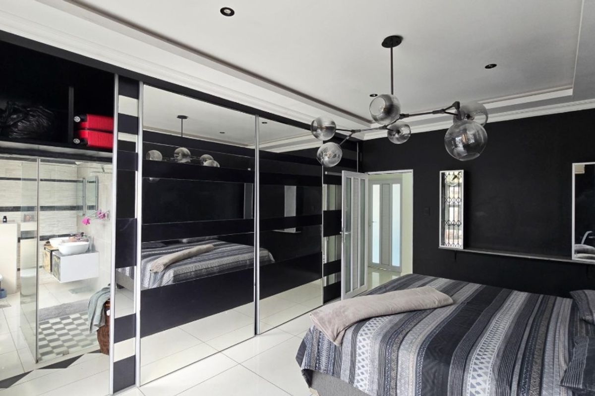 Modern bedroom featuring a large built-in mirrored wardrobe, sleek tiled flooring, and an integrated en-suite bathroom with contemporary fixtures.