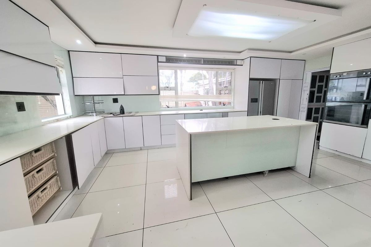 Modern, spacious kitchen featuring white high-gloss cabinetry, a central island, double wall ovens, and large format floor tiles.